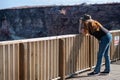 Female tourist watching wildlife and nature through her binoculars. Cliff behind. Wooden floor and handrail. Red hair woman