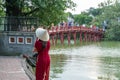 Female tourist wearing Vietnamese traditional dress Ao Dai with The Huc bridge at Hoang Kiem lake on background