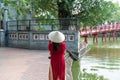 Female tourist wearing Vietnamese traditional dress Ao Dai with The Huc bridge at Hoang Kiem lake on background