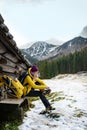 A female tourist in a yellow down jacket puts yellow crampons on her shoes.