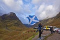 A Female Tourists being photographed holding a Scottish Saltire at the car park in Glen Coe