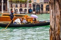 Female tourists on a famous gondola boat ride during rain in the city with Gondolier wearing straw hat, standing with rowing oar.