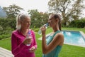 Female trainer and active senior woman drinking water in the backyard