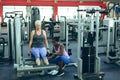 Female trainer assisting active senior woman to work out on leg curl machine Royalty Free Stock Photo