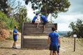 Female trainer assisting fit man to climb over wooden wall during obstacle course Royalty Free Stock Photo