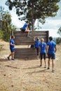 Female trainer assisting fit woman to climb over wooden wall during obstacle course Royalty Free Stock Photo