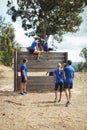 Female trainer assisting fit woman to climb over wooden wall during obstacle course Royalty Free Stock Photo