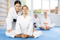 Female trainer helping woman in kimono sit in butterfly pose in gym