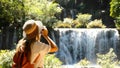 Female travel blogger with photo camera shooting amazing tropical waterfall in Asia journey. Cinematic and inspiration Royalty Free Stock Photo