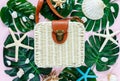 Female traveler accessories on pink background with white stylish fashion rattan bag, shells, tropic monstera leaves, starfish