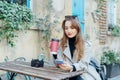 Female traveler chatting, sharing files, resting in cafe terrace table with vintage camera and coffee in reusable cup