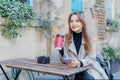 Female traveler chatting, sharing files, resting in cafe terrace table with vintage camera and coffee in reusable cup