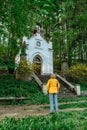 Female traveler looking at small tiny chapel of Our Lady of Lourdes,Broumovsko region,Czech republic.Rural Catholic church in