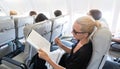 Woman reading magazine on airplane during flight. Female traveler reading seated in passanger cabin.