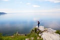 A female traveler stands on a rock and photographs Lake Baikal, the village of Listvyanka on a summer day Royalty Free Stock Photo