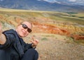 Female traveler takes a selfie sitting on hill on the background of Martian landscapes in Altai mountains. Young girl smiles the Royalty Free Stock Photo