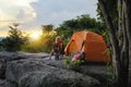 Female Travelers Pitch Vibrant Orange Tent on Cliff with a Natural View. Setting Camping Stove on Cliff, Embracing Pristine