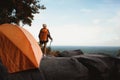Female Travelers Pitch Vibrant Orange Tent on Cliff with a Natural View. Standing Relax on Cliff, Embracing Pristine Natural Views
