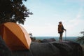 Female Travelers Pitch Vibrant Orange Tent on Cliff with a Natural View. Standing Relax on Cliff, Embracing Pristine Natural Views