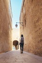 Female traveling alone on the Malta island. Tourist walking by the narrow ancient medieval Mdina streets with a city backpack and