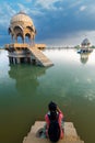 Female traveller photographer shooting Chhatris with reflection on water, dome-shaped pavilions on Gadisar or Gadaria lake. An