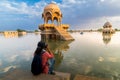 Female traveller photographer shooting Chhatris with reflection on water, dome-shaped pavilions on Gadisar or Gadaria lake. An