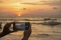 Female traveller taking a dramatic beautiful sunset picture with mobile phone close to Kuta beach in Bali