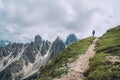 Female trekker walking with backpack and trekking poles by green mountain hill and enjoying the picturesque Dolomite Alps Cinque