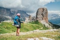 Female trekker walking with backpack and trekking poles by green mountain hill and enjoying the picturesque Dolomite Alps Cinque Royalty Free Stock Photo