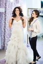 Female trying on wedding dress in a shop with women assistant. Royalty Free Stock Photo