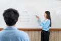 Female tutor standing in front of whiteboard and writing math equations on board to explaining for student Royalty Free Stock Photo