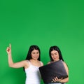 Female twins on a green background. Holding a laptop, points finger up to the empty space. Technology and advertisment