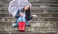 Female with an uncertain face expression sits on the stairs outdoors, holding umbrella in one hand and checking rain drops by the Royalty Free Stock Photo