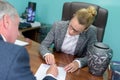 female undertaker asking client to sign paperwork urn on desk