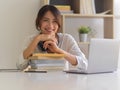 Female university student smiling to camera while sitting at study table with laptop and stack of books