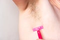 Female unshaved armpits, depilation, hair removal concept. Woman shaves hairy armpit using razor on grey background. Royalty Free Stock Photo