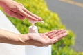 Female using gel sanitizer with green healthy blurry background.