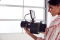 Female Videographer With Video Camera Filming Movie In White Studio