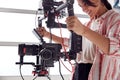 Female Videographer With Video Camera On Steady Cam Rig Filming Movie In White Studio