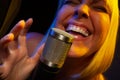 Happy female vocalist under gelled lighting sings with passion into condenser microphone