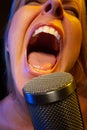 Big mouthed female vocalist under gelled lighting sings with passion into condenser microphone