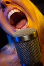 Big mouthed female vocalist under gelled lighting sings with passion into condenser microphone