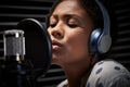 Female Vocalist Wearing Headphones Singing Into Microphone In Recording Studio