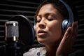 Female Vocalist Wearing Headphones Singing Into Microphone In Recording Studio