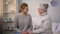 Female volunteer and happy retired lady looking each other sitting hospital bed Royalty Free Stock Photo