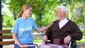 Female volunteer holding book spending time with handicapped elderly man at park