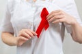 A female volunteer at lab coat attaches a red ribbon to her chest. Close up. The concept of world AIDS day