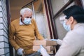 Female volunteer in mask gives an elderly man boxes with food near his house. Quarantined, . Coronavirus covid-19.