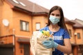 Female volunteer in protective mask and gloves with products on street. Aid during coronavirus quarantine