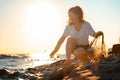 A female volunteer squats and picks up plastic bottles on the ocean shore. Copy space. Cleaning of the coastal zone Royalty Free Stock Photo